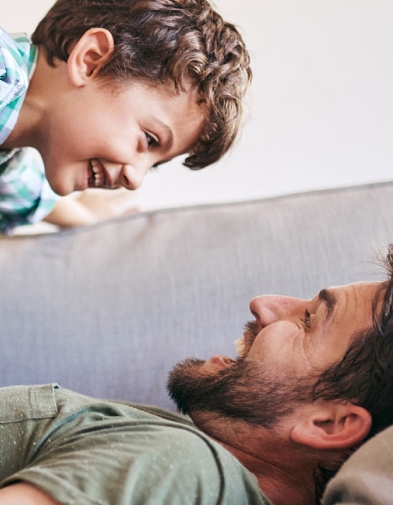 Father and young child playing together on a couch.