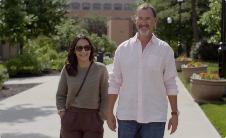 Father and adult daughter walking outdoors on sunny day.