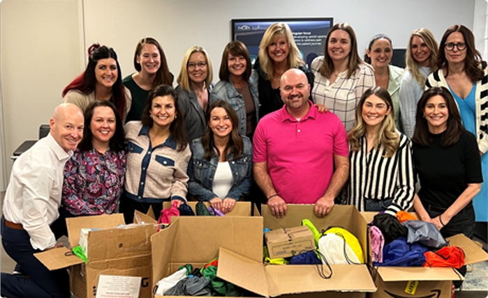 Group of people smiling behind open boxes filled with colorful bags and supplies.