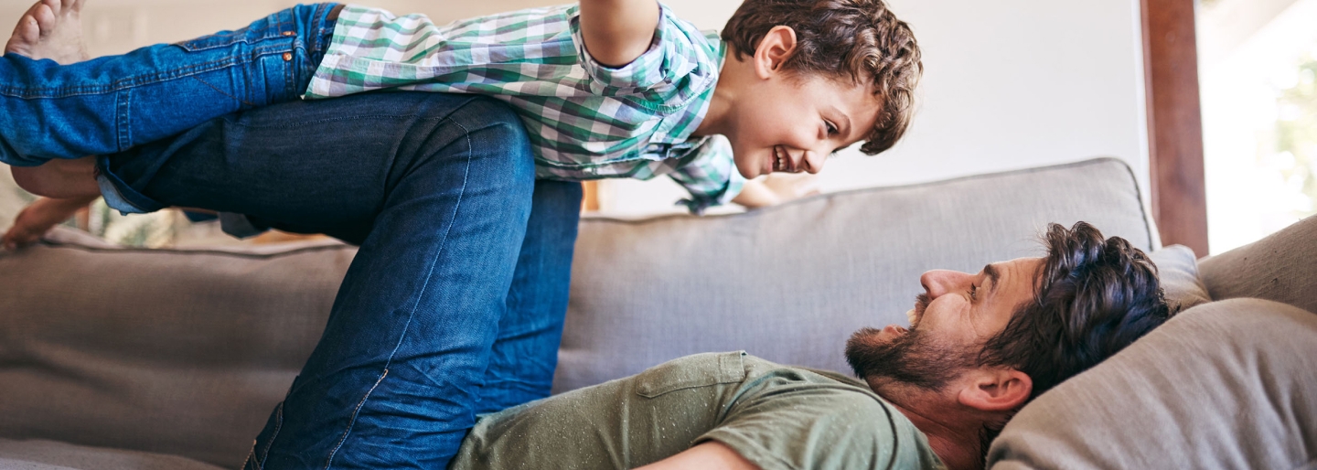 Father and young child playing together on a couch.