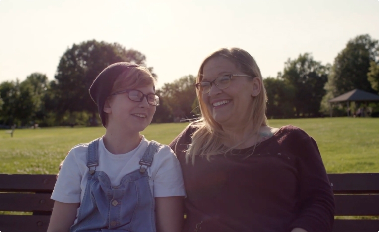 Mother and daughter smiling on a park bench.