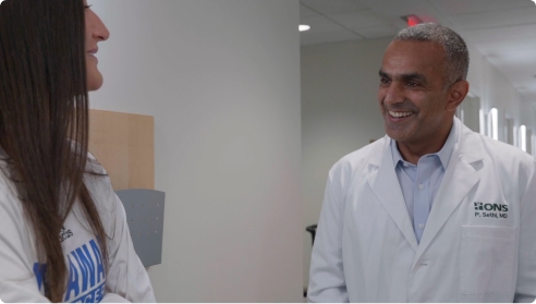 Video thumbnail of a doctor in a lab coat talking to a woman in a young patient in a hallway.