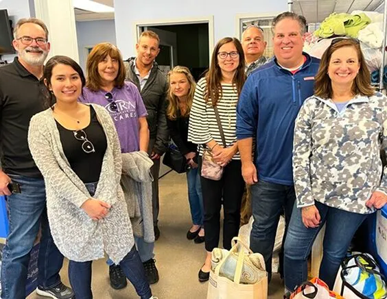 Group of volunteers indoors, smiling and gathered with donated supplies.