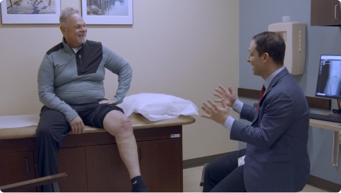Video thumbnail showing a patient with gray hair sitting on an exam table, talking with a physician.